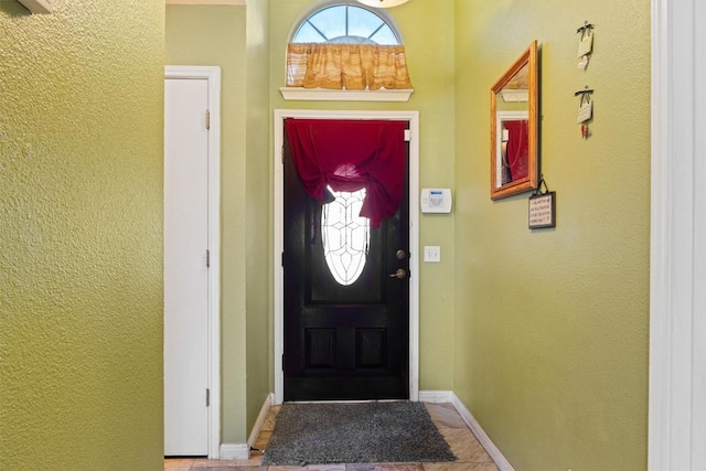 tiled entryway with a textured wall and baseboards
