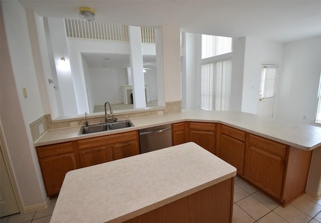 kitchen with a sink, light tile patterned floors, a peninsula, light countertops, and stainless steel dishwasher