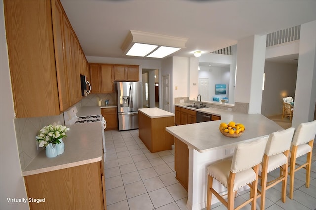 kitchen featuring a breakfast bar area, a sink, stainless steel appliances, light countertops, and a peninsula