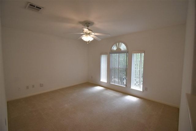 carpeted spare room featuring baseboards, visible vents, and ceiling fan