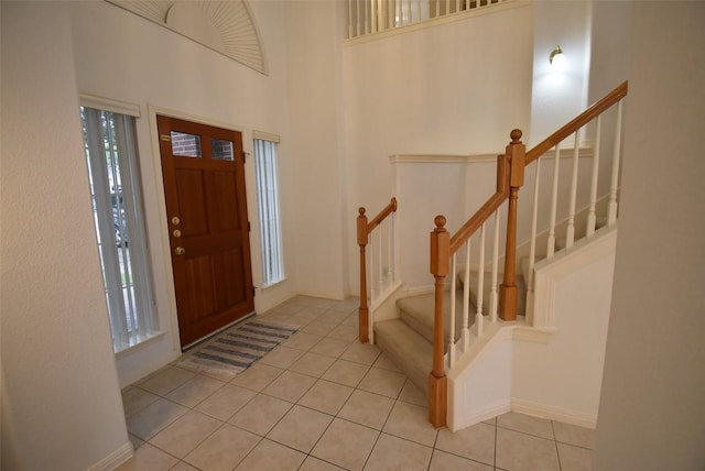 tiled entryway with baseboards, a wealth of natural light, stairs, and a towering ceiling