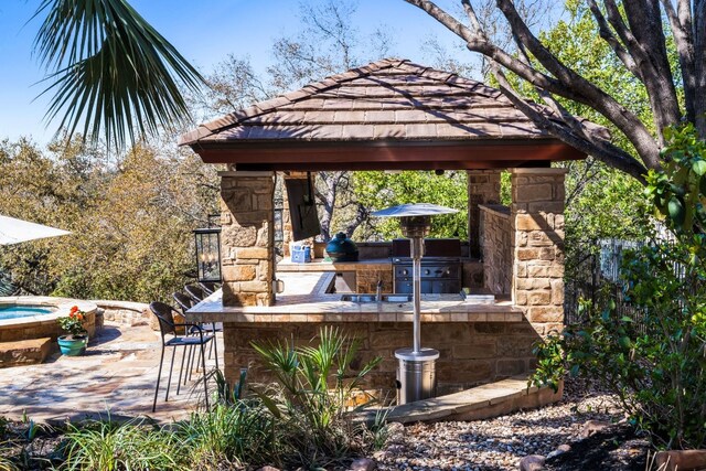 view of patio featuring exterior bar, an outdoor kitchen, a gazebo, a hot tub, and a grill