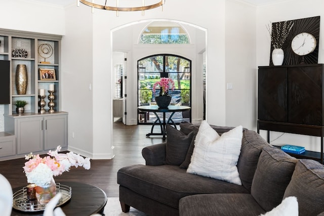 living room featuring wood finished floors, crown molding, baseboards, and arched walkways