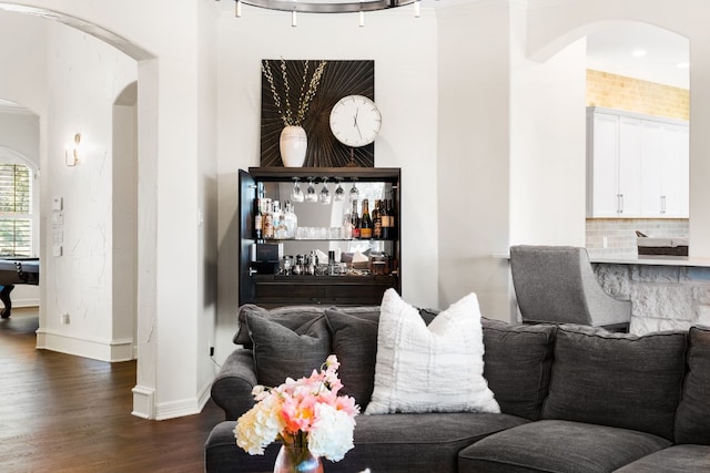 living area with dark wood-style floors, arched walkways, a bar, and baseboards