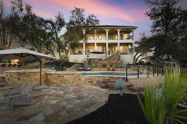back of house at dusk with stairs, an outdoor pool, a patio area, and a balcony