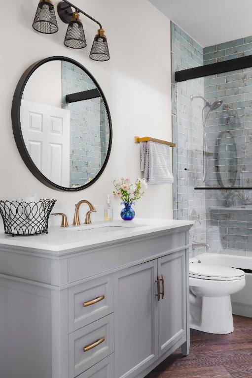 full bath featuring a tile shower, wood finished floors, toilet, and vanity