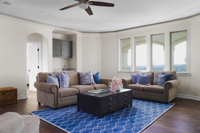 living area with arched walkways, ornamental molding, wet bar, a ceiling fan, and dark wood-style floors