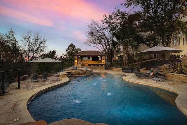 pool at dusk with a patio, outdoor dry bar, and an outdoor pool