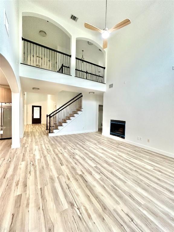 313 El Socorro Ln, Austin, TX 78732 - unfurnished living room with visible vents, a fireplace, ceiling fan, stairway, and light wood finished floors