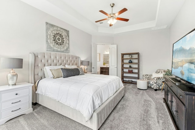 bedroom featuring connected bathroom, light carpet, visible vents, a ceiling fan, and a tray ceiling