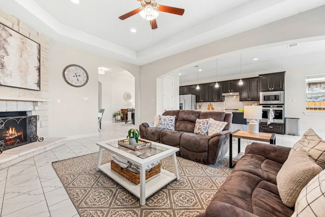 living area featuring a stone fireplace, ceiling fan, arched walkways, recessed lighting, and marble finish floor