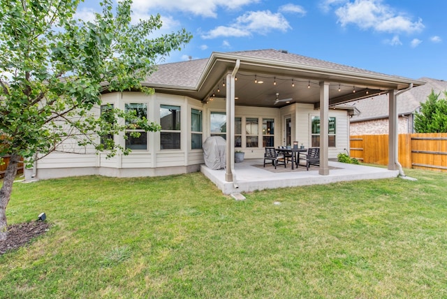 rear view of house with a patio, roof with shingles, a lawn, fence, and a ceiling fan