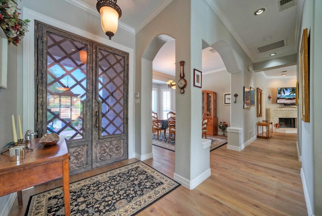 foyer entrance with arched walkways, light wood-style floors, ornamental molding, baseboards, and visible vents