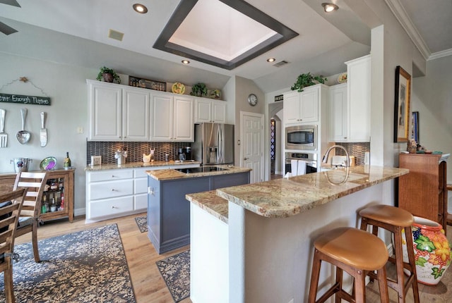 kitchen featuring tasteful backsplash, a center island, a peninsula, white cabinets, and appliances with stainless steel finishes