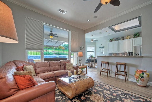 living area with crown molding, ceiling fan, light wood-style floors, and visible vents