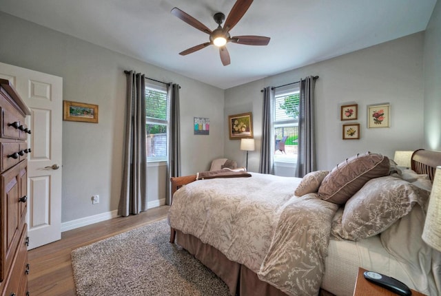 bedroom featuring wood finished floors, baseboards, a ceiling fan, and multiple windows