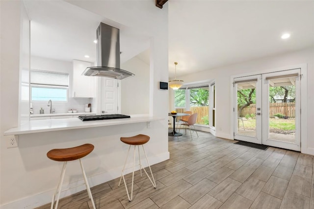 7310 Broken Arrow Ln, Austin, TX 78745 - kitchen with a kitchen breakfast bar, white cabinetry, light countertops, black cooktop, and island exhaust hood