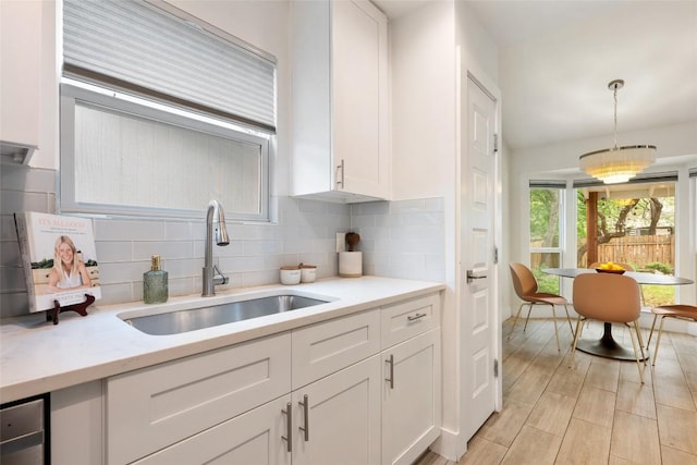 7310 Broken Arrow Ln, Austin, TX 78745 - kitchen with light wood-style flooring, backsplash, a sink, white cabinetry, and pendant lighting