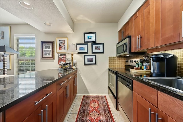 7685 Northcross Dr Unit 304, Austin, TX 78757 - kitchen with stainless steel appliances, backsplash, dark stone counters, light tile patterned floors, and brown cabinets