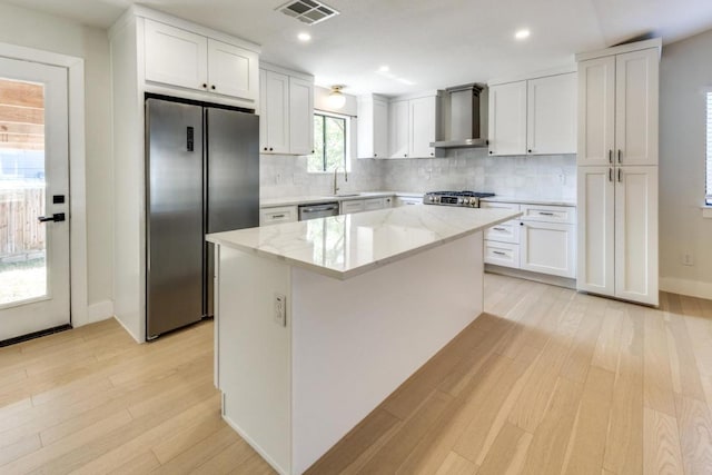 7901 Keswick Dr, Austin, TX 78745 - kitchen with wall chimney range hood, stainless steel appliances, a sink, light wood-type flooring, and white cabinets