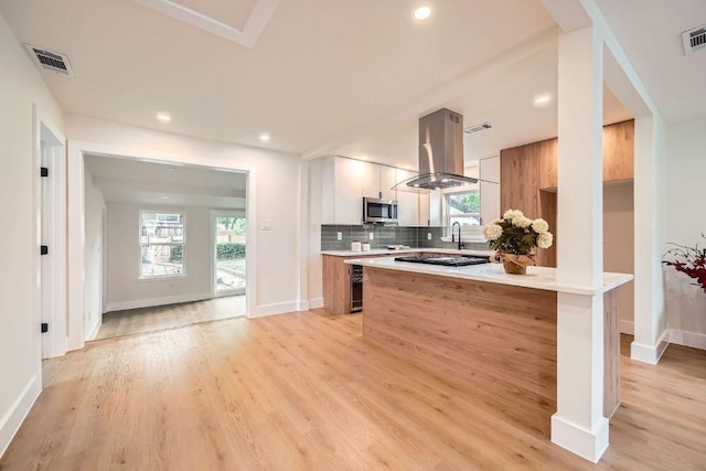 kitchen with visible vents, modern cabinets, island range hood, stainless steel microwave, and a wealth of natural light