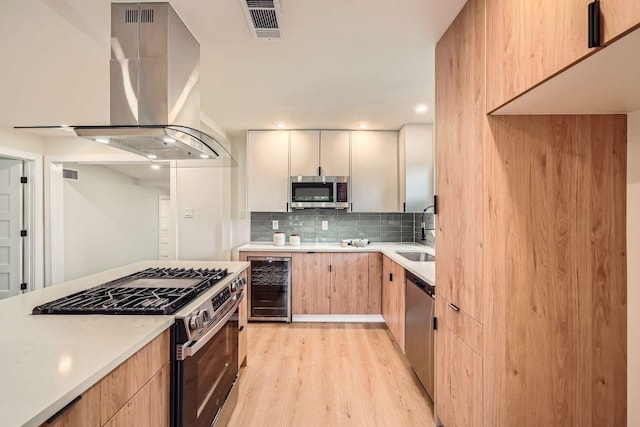 kitchen with appliances with stainless steel finishes, island exhaust hood, light wood-type flooring, wine cooler, and visible vents