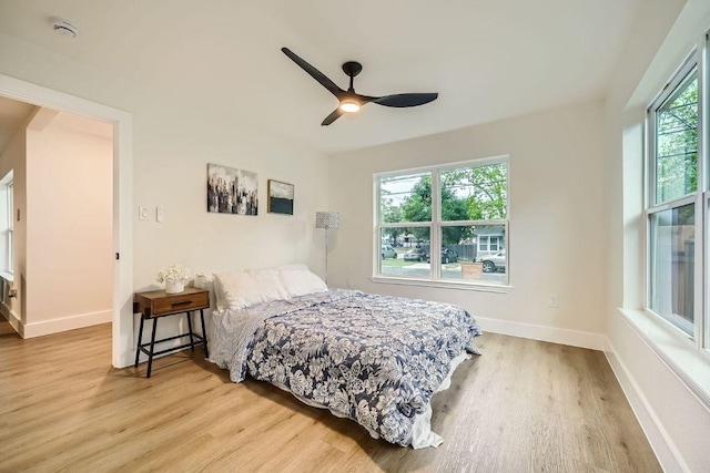 bedroom featuring ceiling fan, baseboards, multiple windows, and wood finished floors