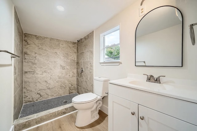 full bathroom featuring vanity, wood finished floors, a tile shower, and toilet