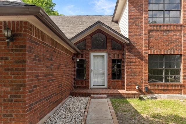 doorway to property with a chimney, a shingled roof, and brick siding