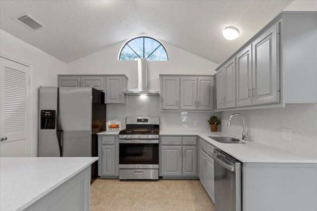 kitchen with appliances with stainless steel finishes, wall chimney range hood, vaulted ceiling, a sink, and gray cabinetry