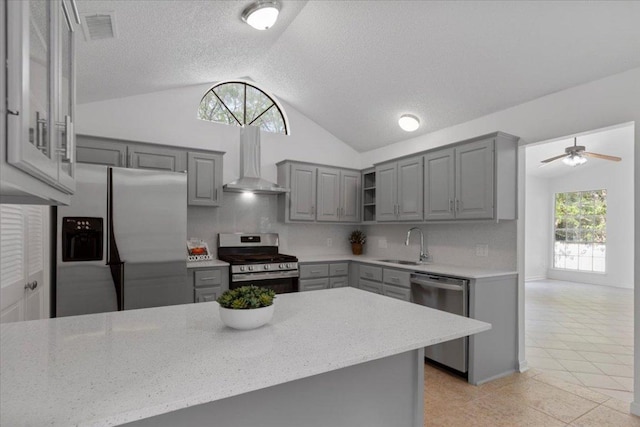 kitchen with gray cabinets, wall chimney exhaust hood, a ceiling fan, appliances with stainless steel finishes, and lofted ceiling