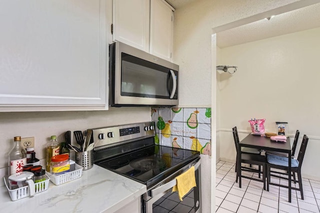 kitchen with light stone counters, light tile patterned floors, white cabinetry, decorative backsplash, and appliances with stainless steel finishes