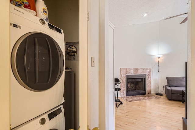 laundry area featuring stacked washer / drying machine, laundry area, light wood-type flooring, a high end fireplace, and a textured ceiling