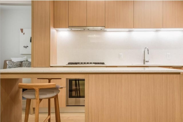 kitchen with a kitchen breakfast bar, beverage cooler, light brown cabinets, and under cabinet range hood