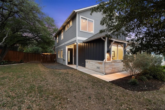 exterior space featuring board and batten siding, a lawn, fence, and stone siding