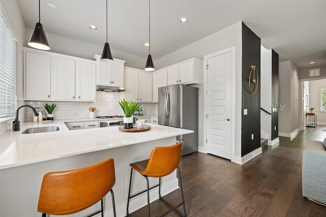 kitchen with a sink, freestanding refrigerator, a peninsula, decorative light fixtures, and tasteful backsplash