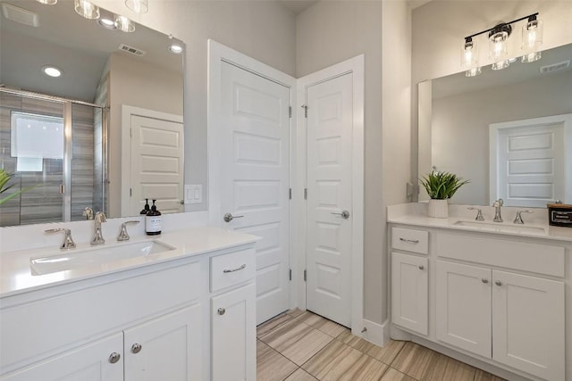bathroom featuring visible vents, two vanities, a sink, and a stall shower