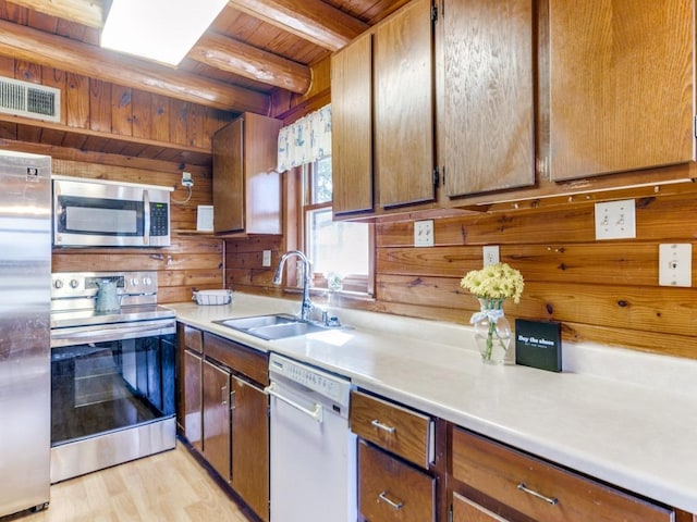 kitchen with a sink, wooden walls, visible vents, wood ceiling, and appliances with stainless steel finishes