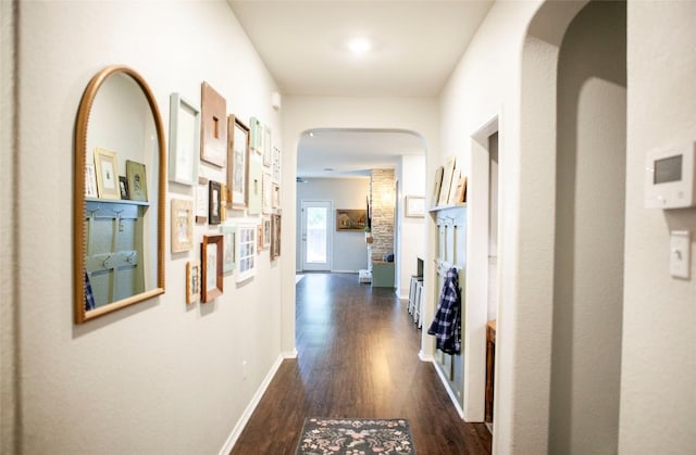 corridor with arched walkways, dark wood-style floors, and baseboards