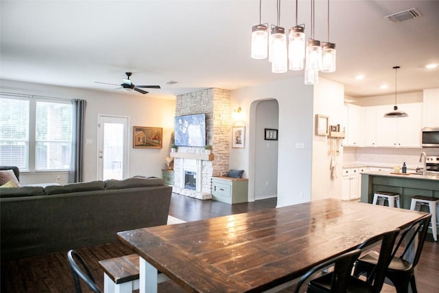 dining area with dark wood-type flooring, visible vents, a ceiling fan, and arched walkways