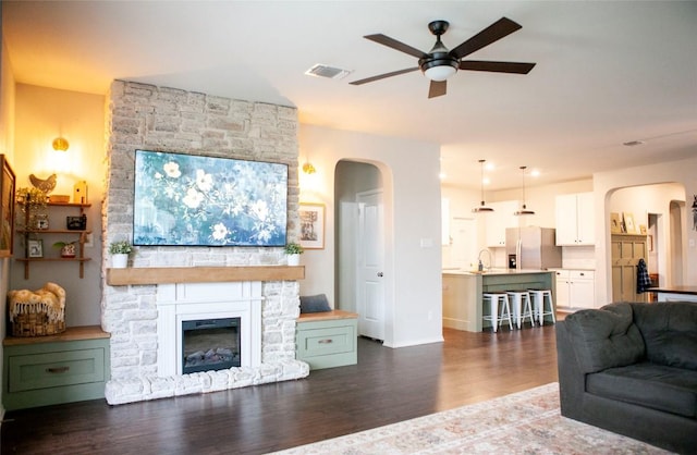 living room featuring dark wood finished floors, arched walkways, a ceiling fan, and a fireplace