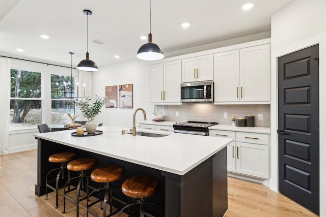 kitchen featuring tasteful backsplash, white cabinets, a sink, stainless steel appliances, and light countertops