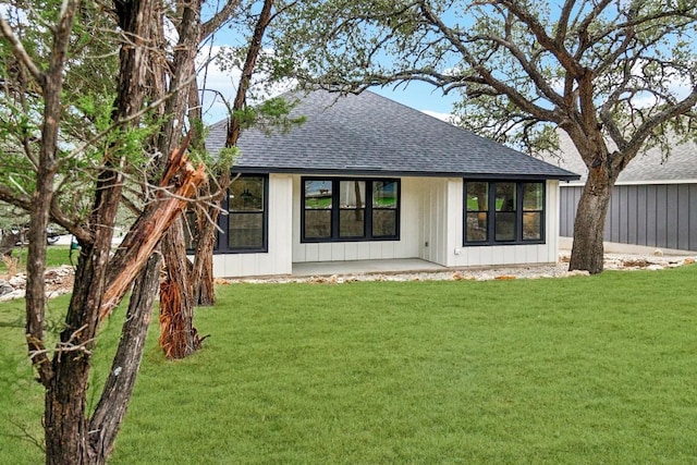 rear view of house with a lawn, board and batten siding, a patio area, and roof with shingles