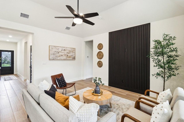 living room featuring a ceiling fan, visible vents, baseboards, and light wood-style floors