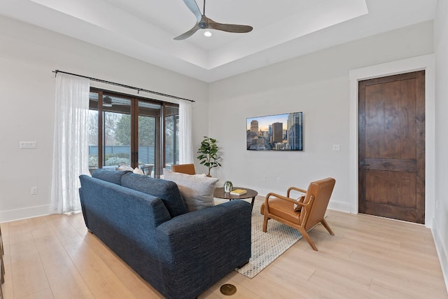 living room featuring baseboards, a ceiling fan, light wood finished floors, and a tray ceiling