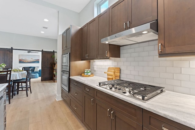 kitchen with decorative backsplash, light countertops, a barn door, under cabinet range hood, and stainless steel appliances