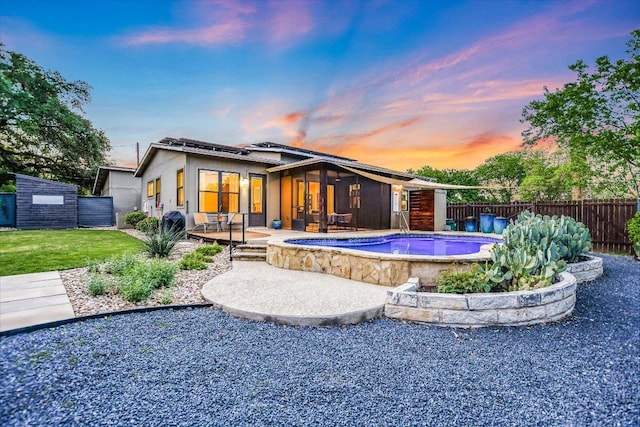 back of house at dusk with a patio, a fenced backyard, an in ground hot tub, and a lawn