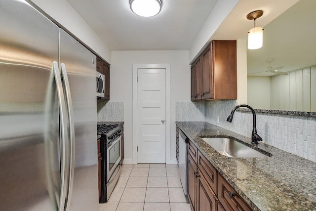 kitchen featuring light tile patterned flooring, dark stone counters, a sink, appliances with stainless steel finishes, and backsplash