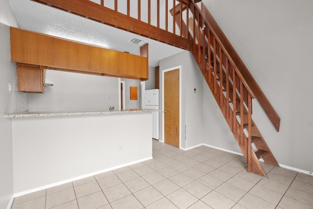 kitchen featuring brown cabinets, light tile patterned floors, visible vents, a peninsula, and baseboards