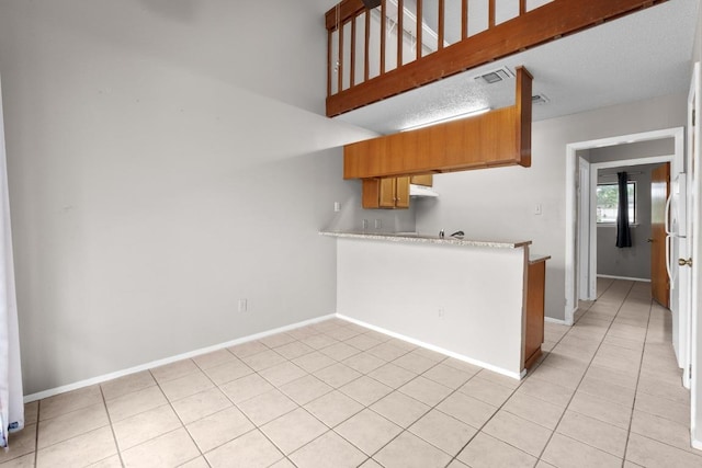 kitchen with light tile patterned floors, light countertops, baseboards, visible vents, and a peninsula